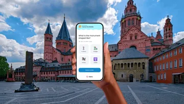 Hand holds phone with riddle game, cathedral backdrop.