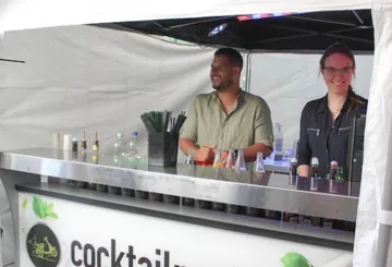 Two bartenders smiling at cocktail bar.