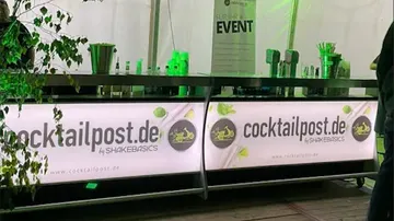 Cocktail bar with foliage and event banner.