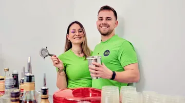 Zwei Personen lächeln hinter einer Bar-Aufstellung.