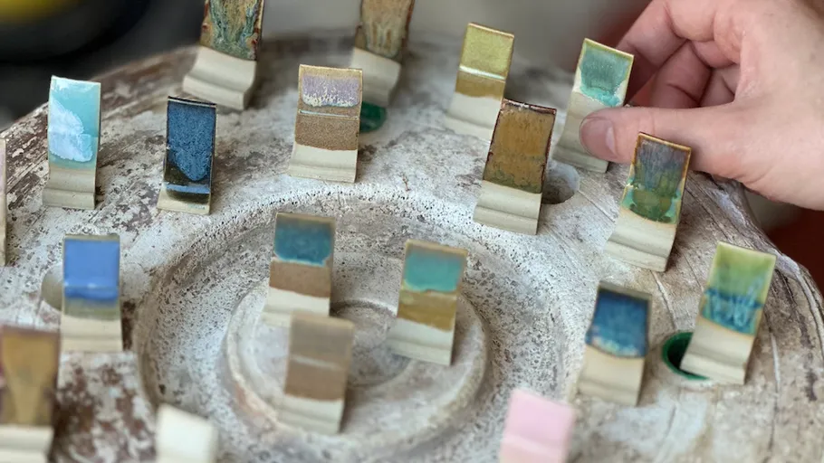 Hand selecting ceramic glaze samples on a tray.