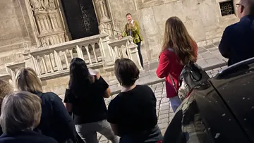 Person speaking outdoors to a small audience.