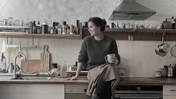 Woman sitting on kitchen counter, holding a mug.