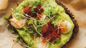 Avocado toast with shrimp and herbs on bread.