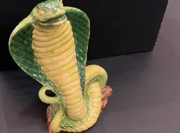 Keramische Kobra-Figur auf schwarzem Untergrund.