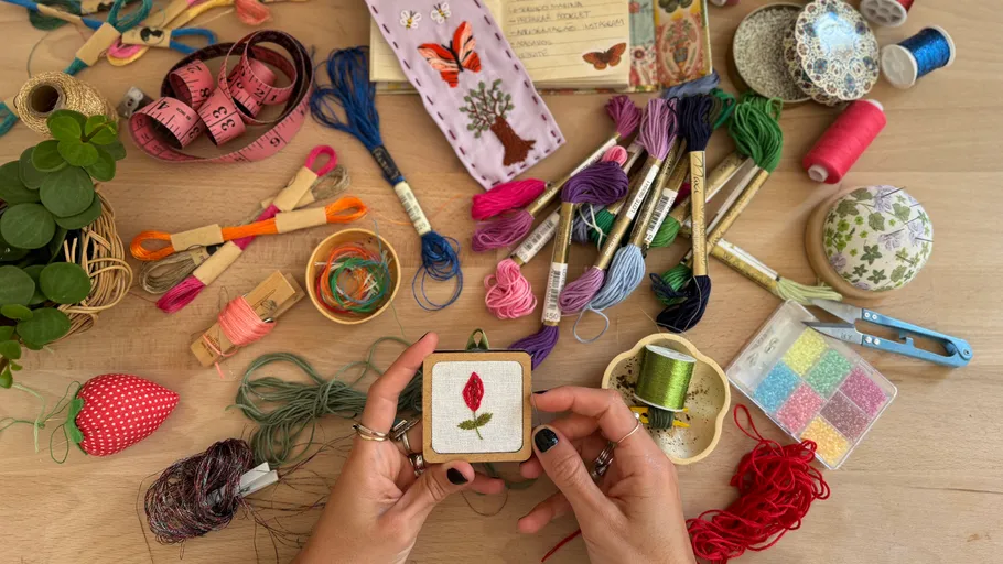 Hands holding embroidery, surrounded by threads.