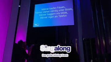 Crowd singing along in purple-lit room.