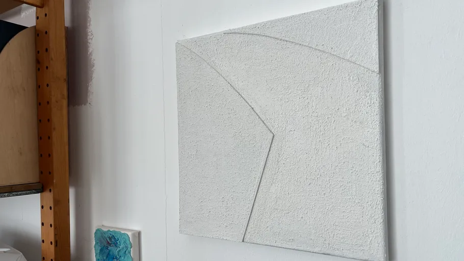 Strukturiertes weißes Kunstwerk an Wand nahe Regal.