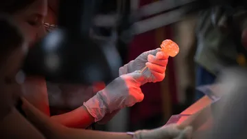 Person examines gemstone under red light in workshop.