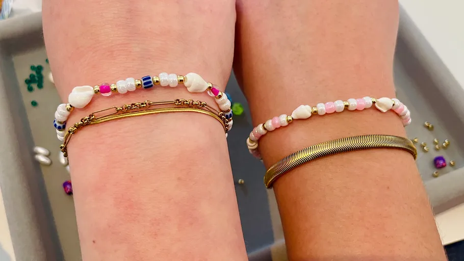 Two wrists wearing colorful beaded bracelets.