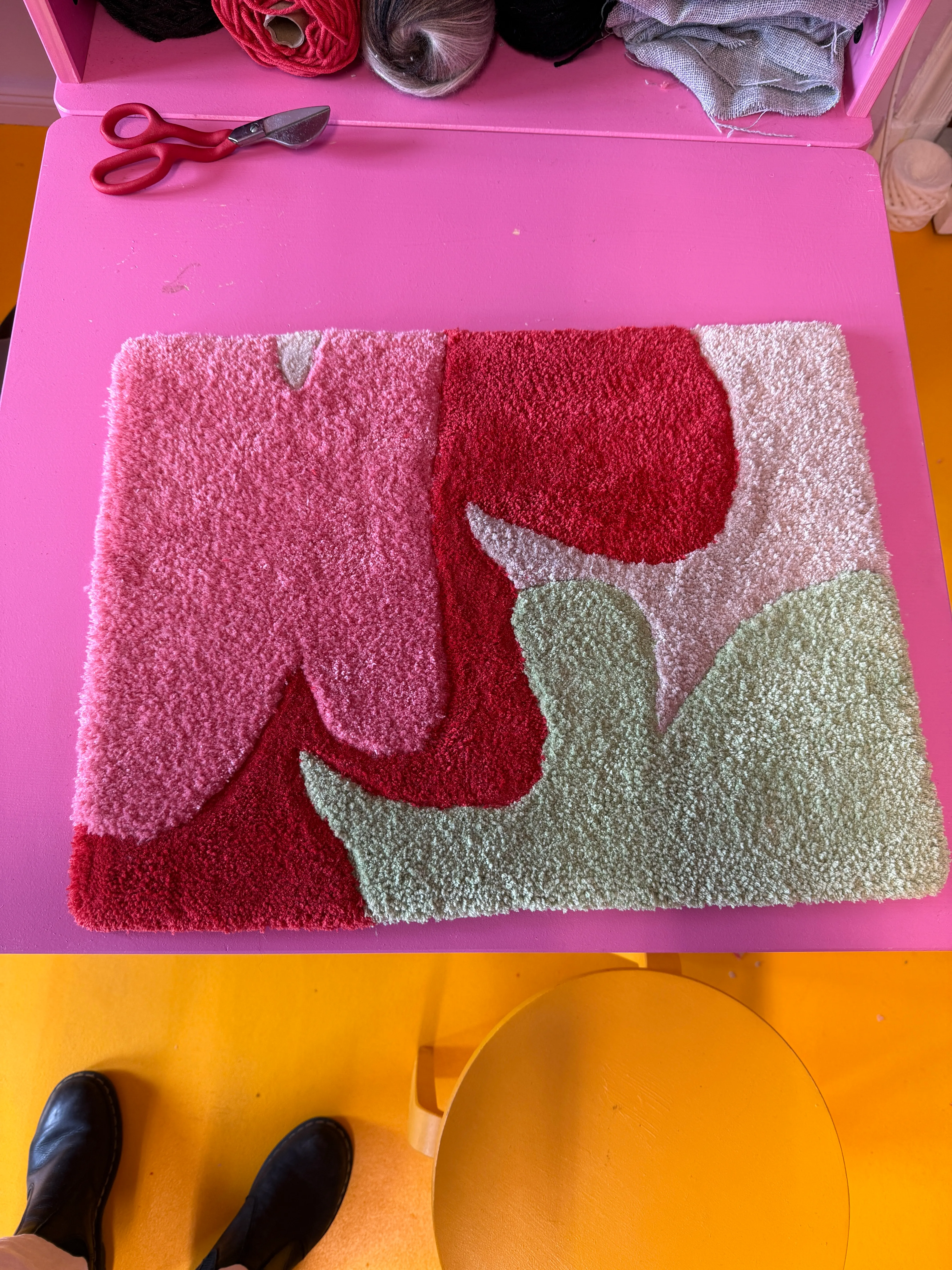 Bunter Teppich auf rosa Tisch in Werkstatt.