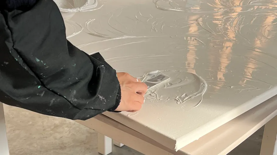 Hand spreading texture on canvas with tool.