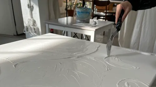 Hand mit Spachtel auf strukturierter Leinwand.