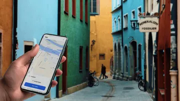 Hand hält Smartphone mit Karte in bunter Gasse.