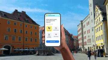 Hand holds phone with quiz in city square.