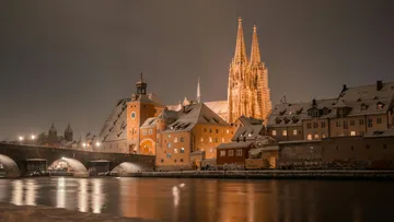 Illuminated cathedral and bridge at night, snowy scene.