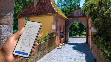 Hand holding phone with map display outdoors.