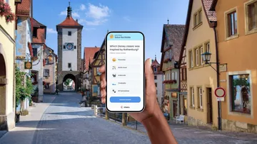Hand holding phone with quiz in German town.
