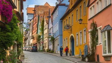 Colorful houses line cobblestone street, people walking.