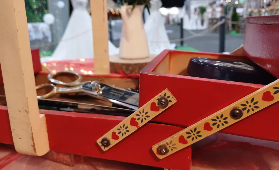 Rote Nähbox mit Scheren, Brautkleider im Hintergrund.