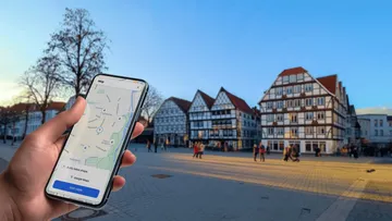Hand hält Telefon mit Karte, historische Gebäude sichtbar.