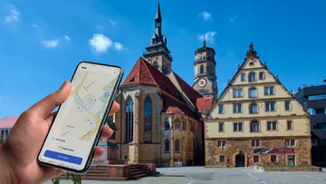 Hand hält Handy mit Karte, Gebäude im Hintergrund.