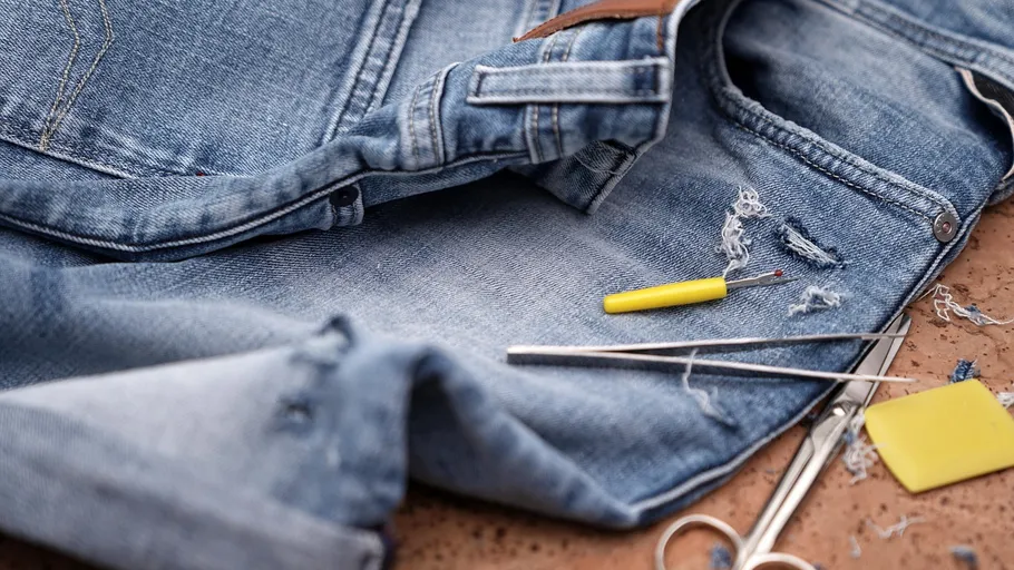 Jeans mit Reparaturwerkzeugen auf Tischplatte.