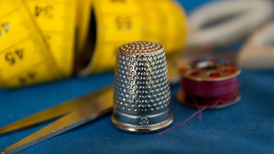 Thimble and sewing tools on blue fabric.