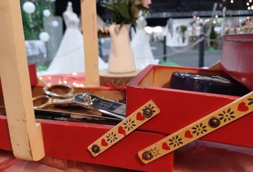 Rote Nähbox mit Scheren, Hochzeitskleider im Hintergrund.