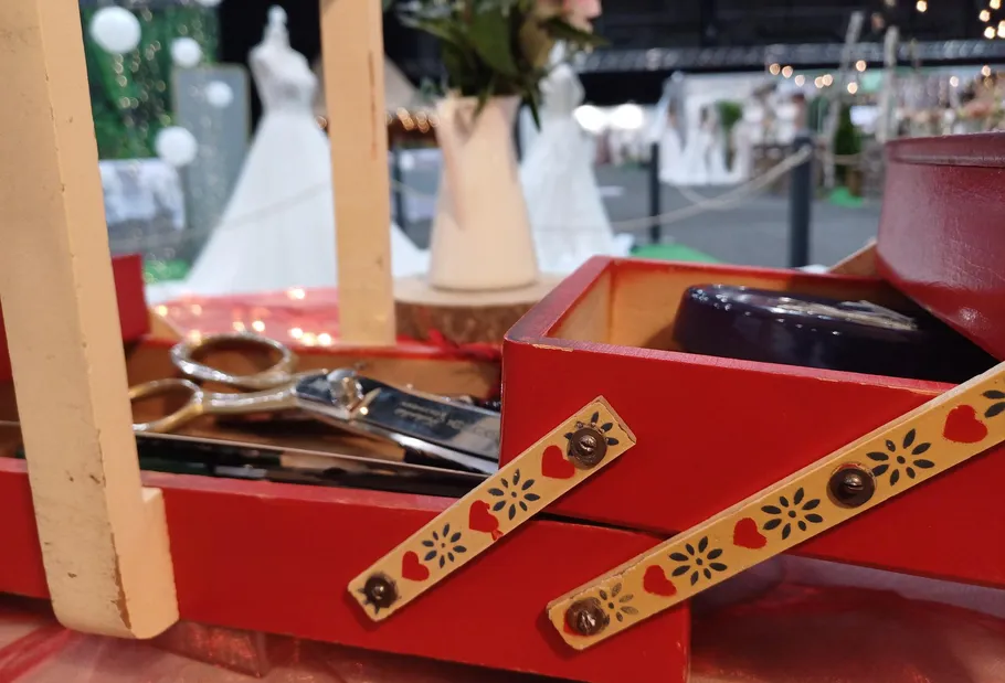 Rote Nähbox mit Scheren, Hochzeitskleider im Hintergrund.