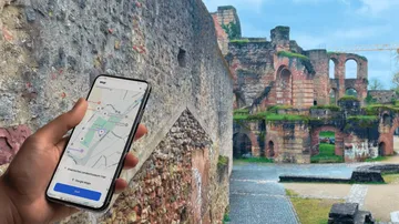 Hand holding phone with map near historical ruins.