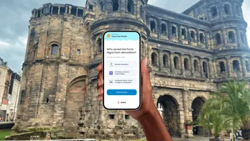 Hand hält Handy mit Quiz vor Monument.