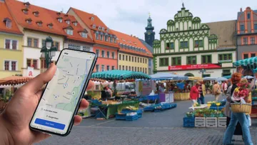 Hand with phone showing map, market background.