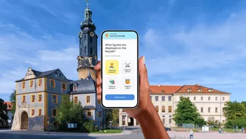 Hand hält Handy mit Quiz nahe historischem Gebäude.