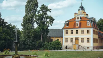 Historisches Herrenhaus mit Brunnen und Bäumen.