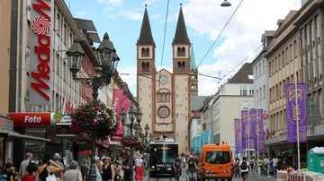 Straßenszene mit Kirchtürmen und Fußgängern.