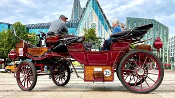 Alte Kutsche fährt auf modernem Stadtplatz.