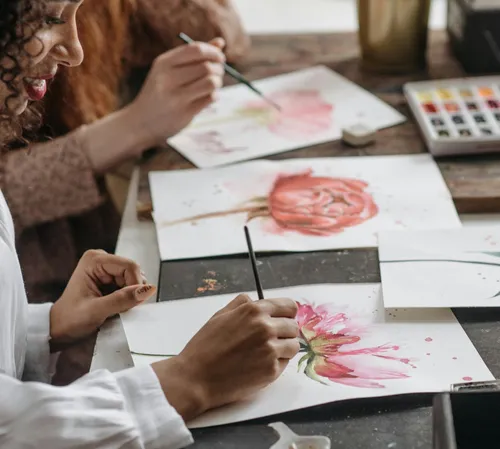 Zwei Personen malen Blumen auf Papier.