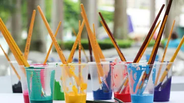 Paintbrushes in colored cups on a table.