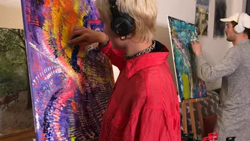 Zwei Künstler malen bunte abstrakte Kunst drinnen.