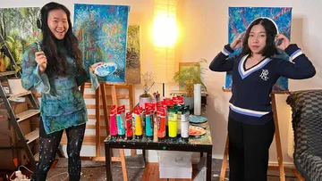Two women wearing headphones, standing in art studio.