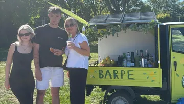 Three people smiling beside colorful drink cart.