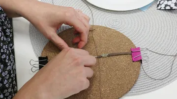 Hands weaving on cork board with clips.