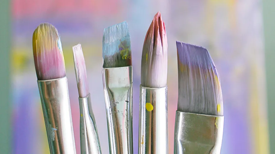 Five paintbrushes with colorful tips, blurred background.