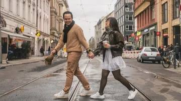 Couple holding hands, walking across city street.