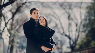 Couple embracing outdoors, trees blurred background.