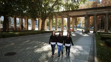 Three people walking in a tree-lined park.