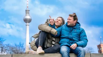 Two people sit smiling, pointing near TV Tower.