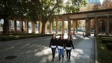 Drei Frauen spazieren in einem sonnigen Park.