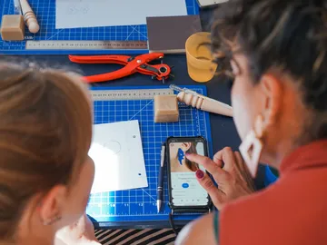 Two women are looking at a smartphone together at a table.
